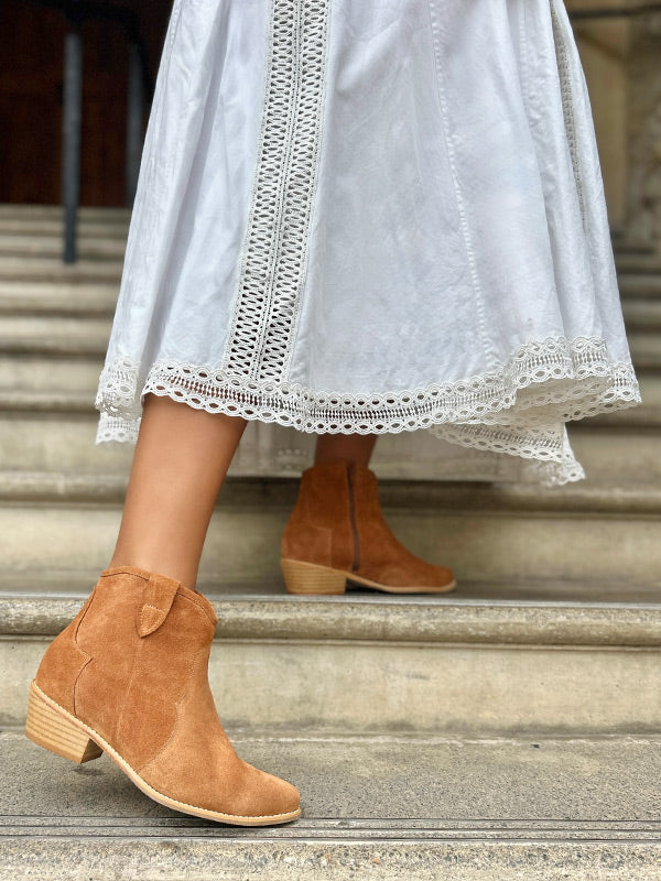 Person wearing brown ankle boots and a white dress with lace details on stone steps.